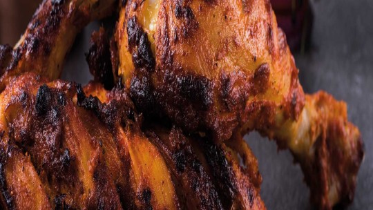 Close-up of grilled tandoori chicken, showcasing the charred and spiced skin with a golden hue.