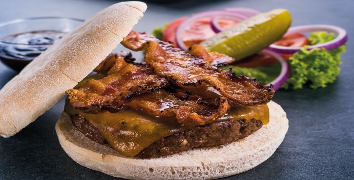 Detailní záběr cheeseburgeru se slaninou a taveným sýrem, podávaného se zeleninou a omáčkou.