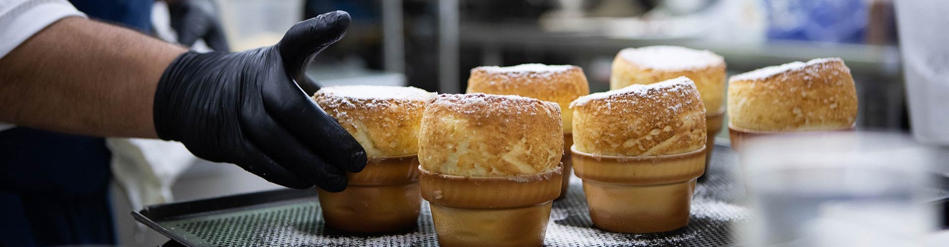 Chef che dispone i soufflé appena sfornati su un vassoio, indossando guanti neri, con sopra lo zucchero a velo.