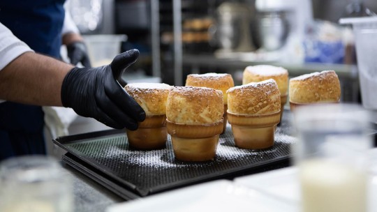 Chef che dispone i soufflé appena sfornati su un vassoio, indossando guanti neri, con sopra lo zucchero a velo.