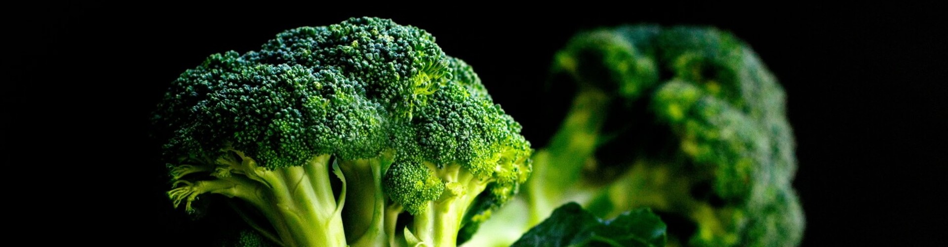 A wooden bowl filled with fresh broccoli against a dark background.