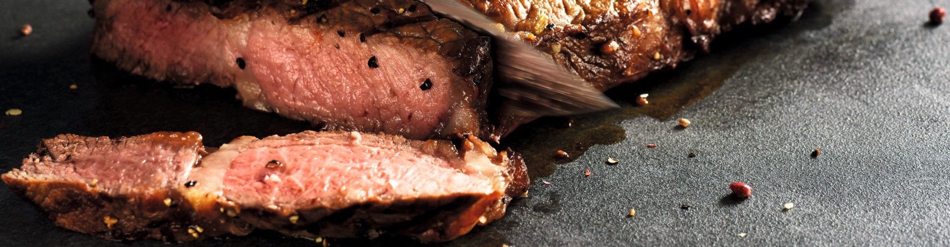 Primo piano di una bistecca di ribeye alla griglia che viene affettata, mettendo in evidenza il succoso interno rosa e il condimento in cima.