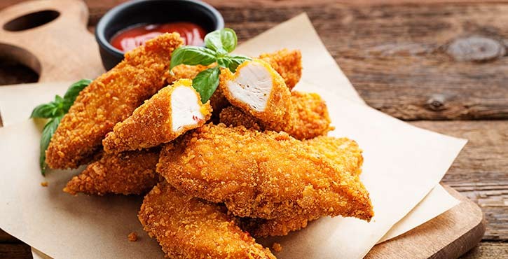 Un plateau de nuggets de poulet dorés avec une sauce de trempage, garnis de feuilles de basilic frais sur une table en bois rustique.