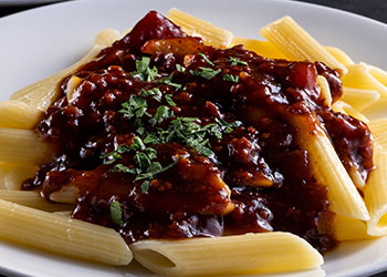 A plate of penne pasta topped with a rich bolognese sauce and garnished with chopped herbs.