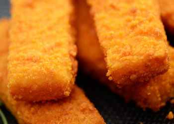 A close-up of crispy golden fish sticks stacked on a dark surface.
