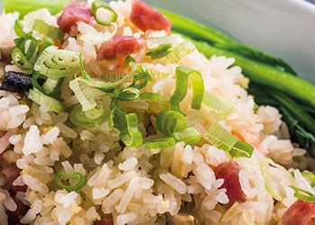 A close-up of fried rice, garnished with chopped spring onions and pieces of meat.