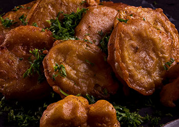 A close-up of crispy fried vegetable fritters garnished with fresh herbs.