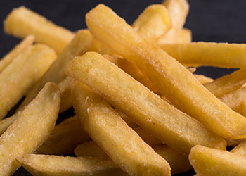 A close-up of crispy golden French fries stacked on a dark surface.