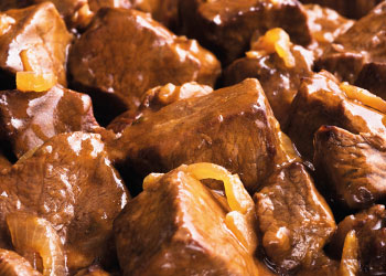 A close-up of tender beef cubes in a rich brown sauce, garnished with onions.