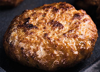 A close-up of a grilled hamburger patty with a golden-brown crust.