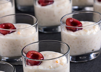 A close-up of small glasses filled with creamy rice pudding topped with cherries.