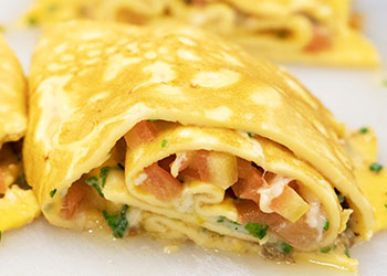 A close-up of a rolled omelette filled with vegetables, herbs, and ham.