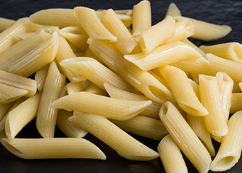 A close-up of penne pasta arranged on a dark surface.