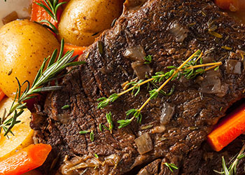 A close-up of a pot roast with tender meat, potatoes, and carrots, garnished with fresh herbs.