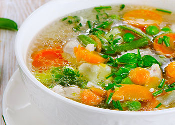 A bowl of vegetable soup filled with various vegetables and herbs in a clear broth.