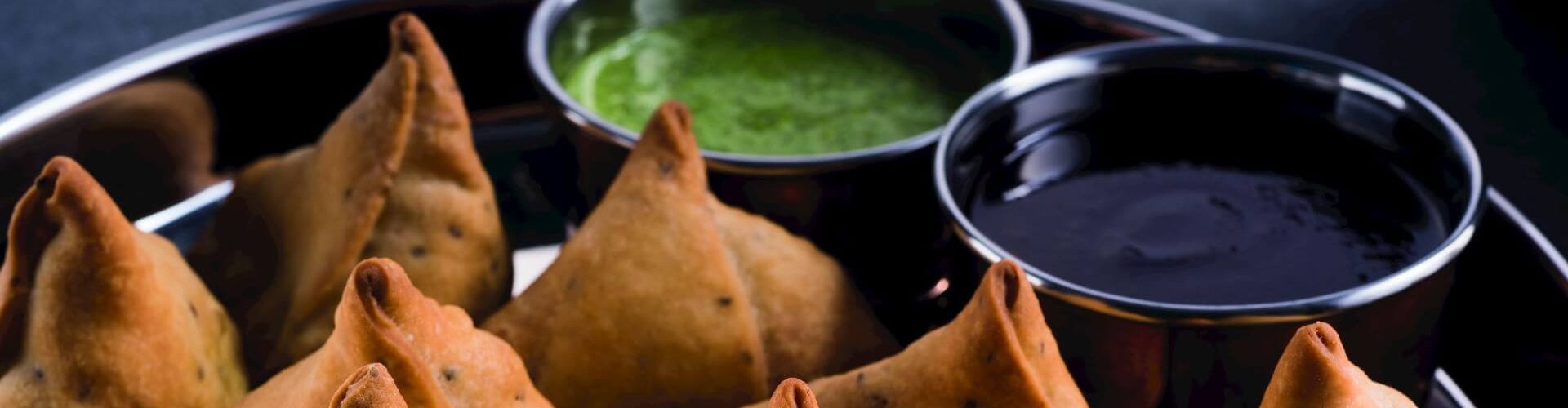 A plate of freshly fried samosas served with green and tamarind sauces on the side.