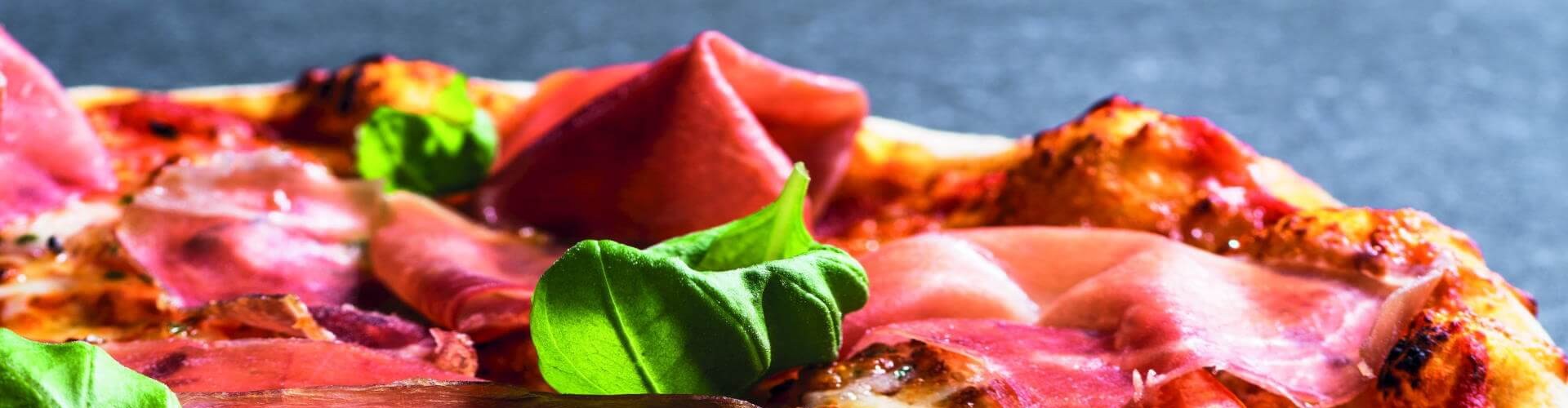 A close-up of a pizza topped with slices of ham and fresh basil leaves, showcasing the vibrant colors and textures of the ingredients.