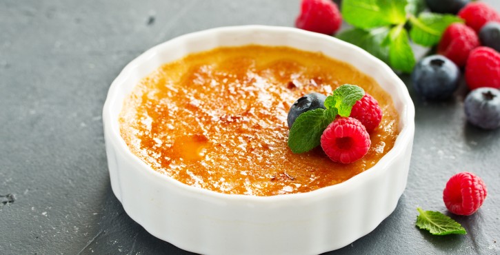 Une crème brûlée crémeuse garnie de framboises et de myrtilles fraîches, agrémentée de feuilles de menthe.