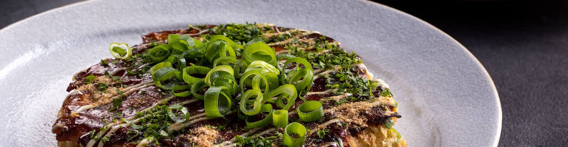 Pięknie podane Okonomiyaki z pokrojoną zieloną cebulką i skropione sosem, prezentujące bogate tekstury i kolory.