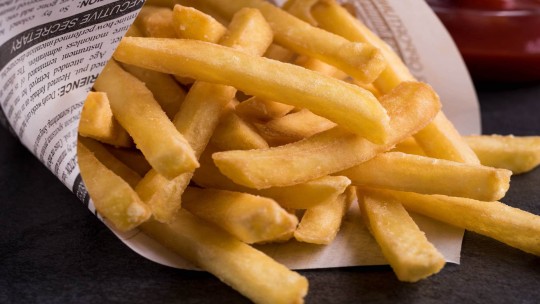 Primo piano di patatine fritte dorate in un cono di carta, accompagnate da ketchup.