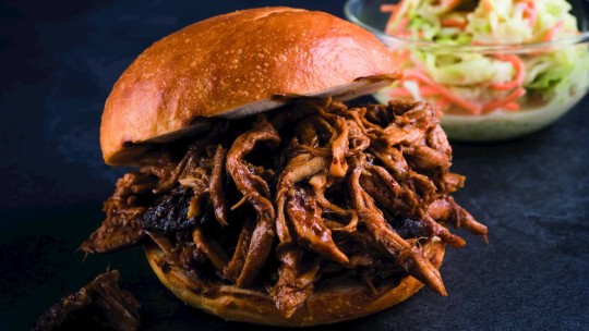 Primo piano di un panino con carne di maiale sminuzzata e salsa barbecue, servito con insalata di cavolo a parte.