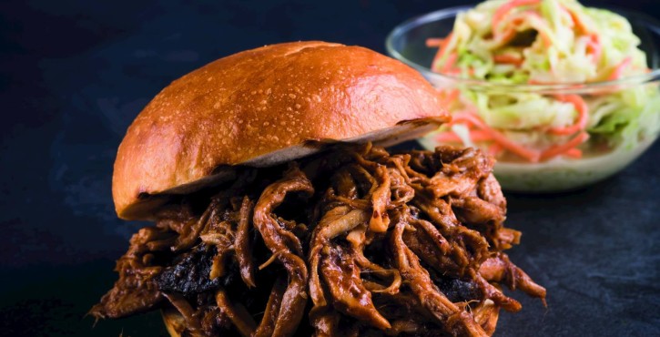Primer plano de un sándwich de cerdo desmenuzado con salsa barbacoa, servido con ensalada de col al lado.
