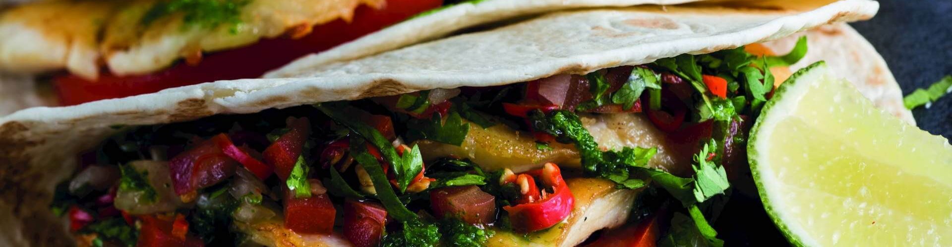 Close-up of fish tacos filled with fried fish, fresh salsa, and garnished with lime wedges.