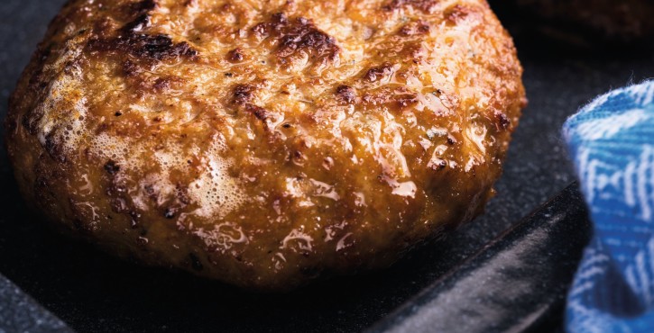 Un gros plan sur une galette de hamburger grillée, montrant sa surface caramélisée et sa texture juteuse.