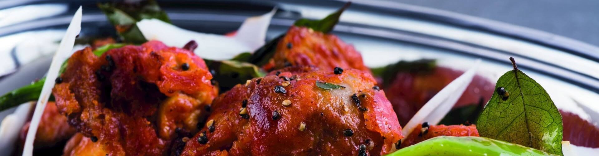 A flavorful dish featuring spiced chicken pieces, garnished with green chilies and fresh herbs, served in a traditional bowl.