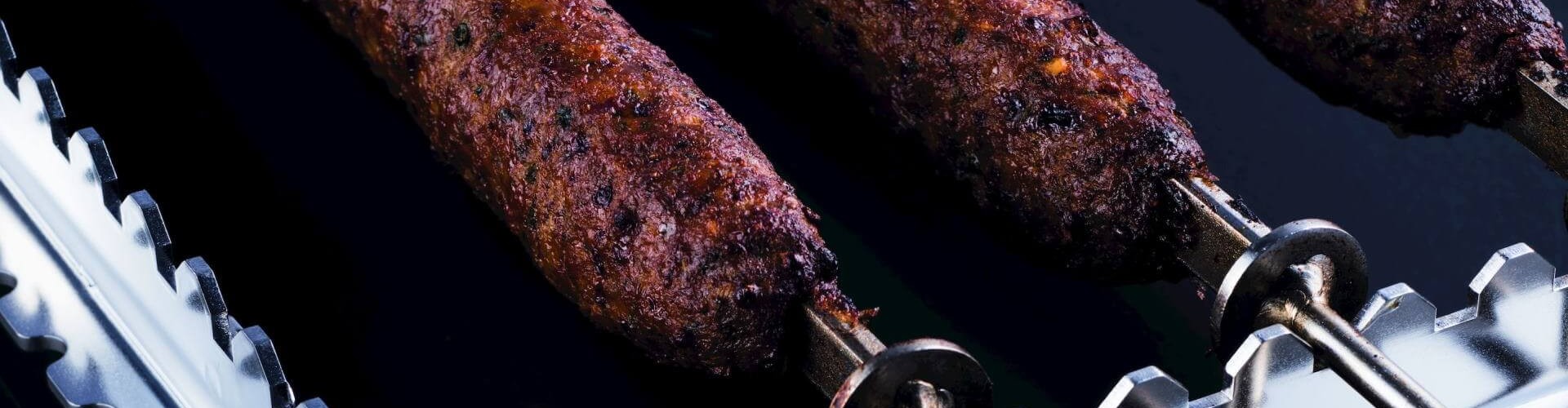 A platter of grilled sheek kebabs, skewered and perfectly cooked, showcasing a rich brown color with spices, resting on a metal rack.