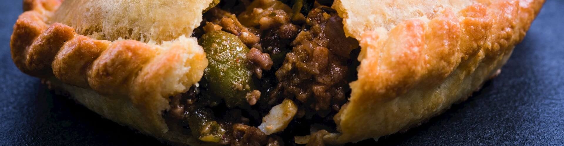 Una empanada recién horneada con una corteza dorada, parcialmente abierta para revelar un relleno sabroso de carne molida y verduras.