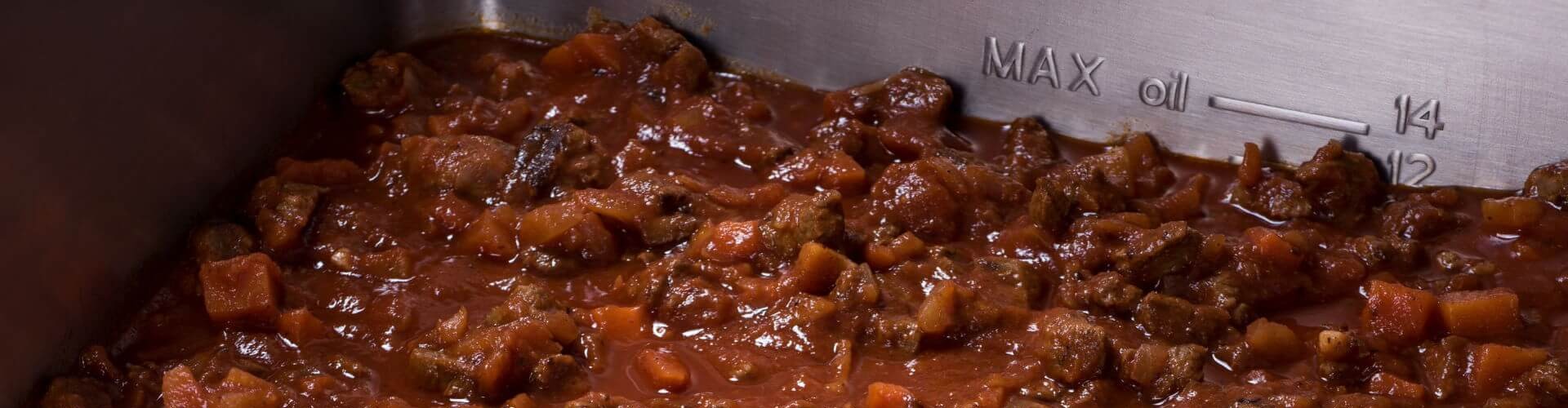 Eine Nahaufnahme eines köchelnden Bolognese-Ragouts mit zarten Rindfleischstücken und gewürfeltem Gemüse in einer reichhaltigen Tomatensauce.