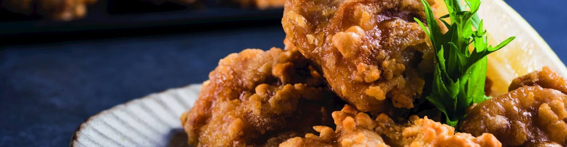 A close-up of crispy Japanese karaage chicken served on a plate with a slice of lemon and greens.