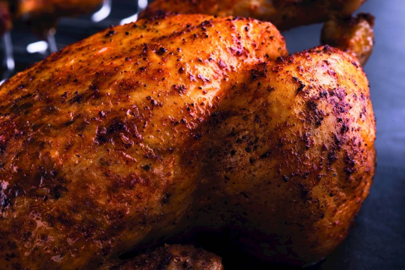 Primo piano di un pollo perfettamente grigliato, che mostra la sua pelle croccante e dorata e la sua consistenza succosa.