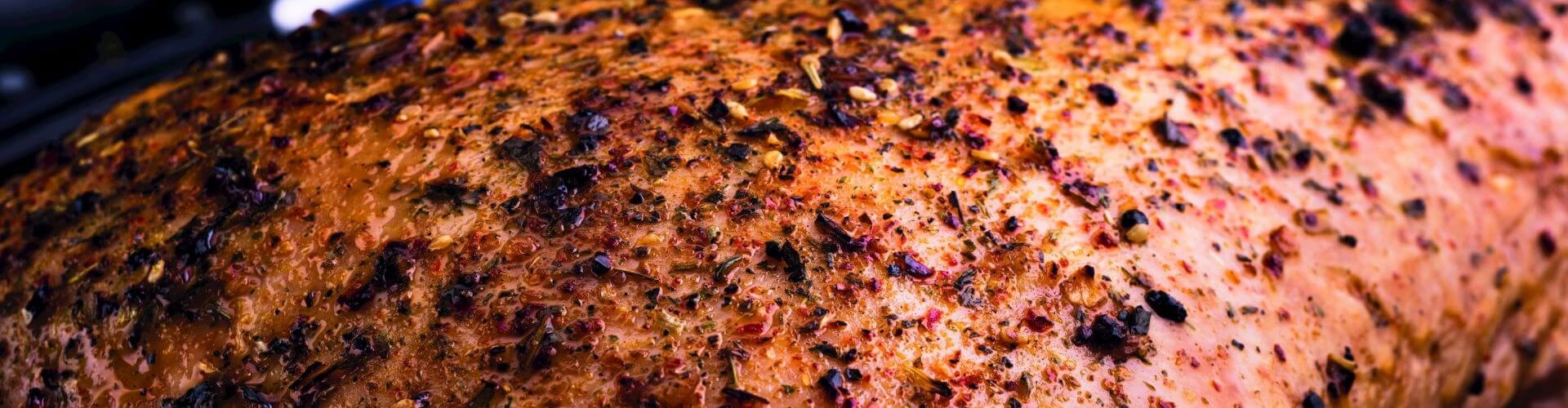 Eine Nahaufnahme eines gewürzten Putenbratens mit einer goldbraunen Kruste und Kräutern, der auf einer Kochfläche ruht.
