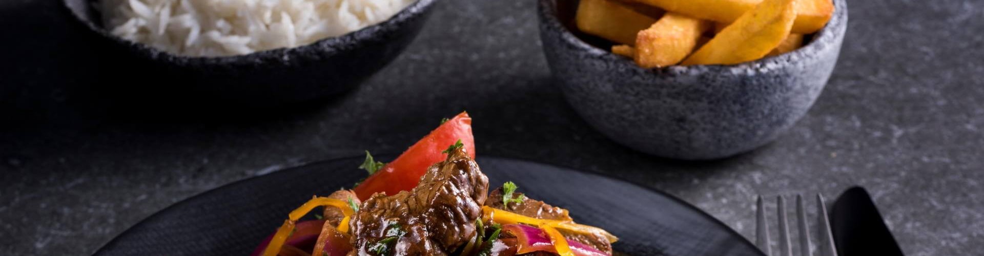 Plate of lomo saltado with beef, tomatoes, and colorful vegetables, served with rice and fries.