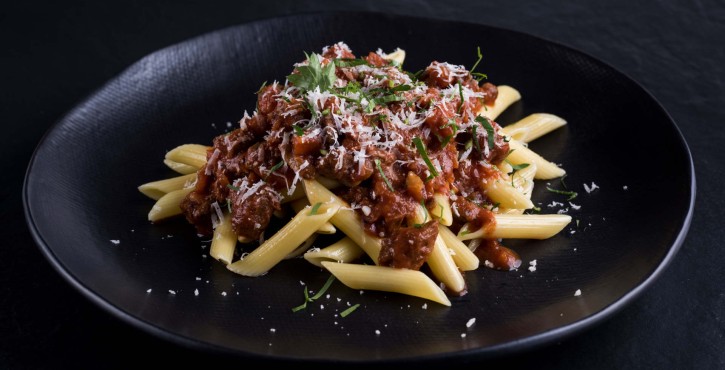  A plate of penne pasta topped with a rich meat sauce, garnished with grated cheese and fresh herbs.