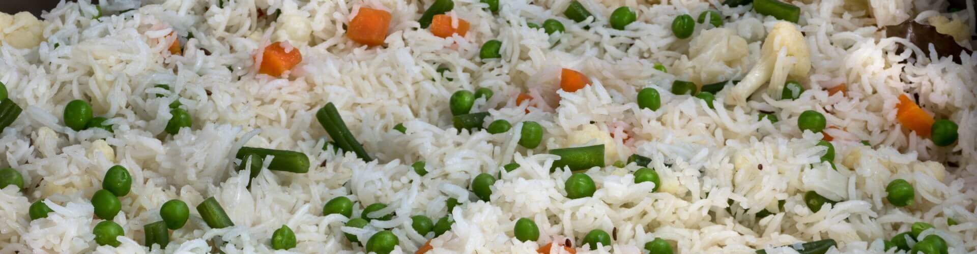 A large pan of colorful vegetable pulao, featuring fluffy white rice mixed with green peas, carrots, and cauliflower.