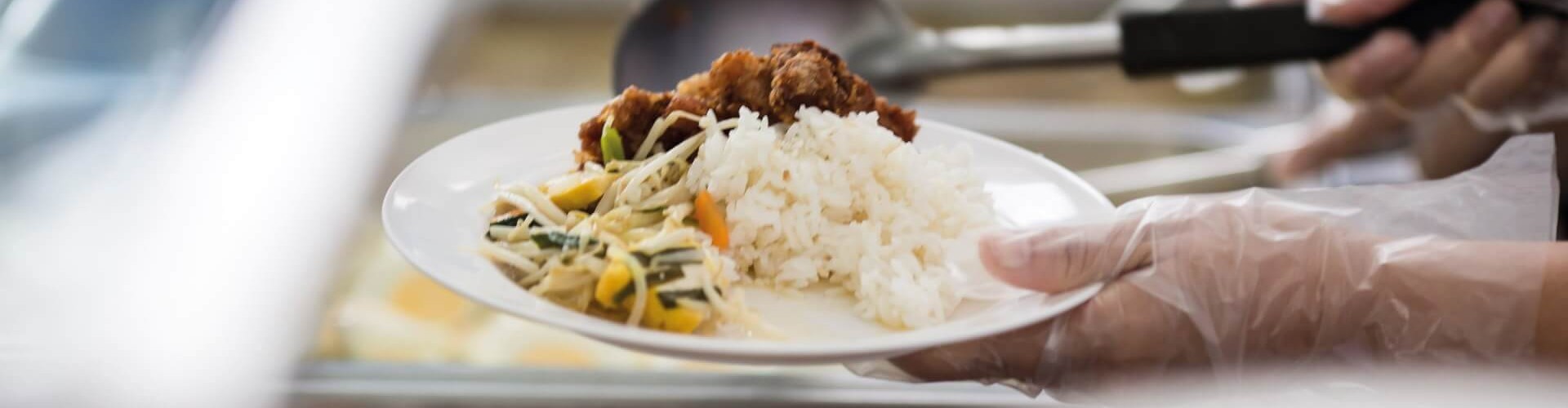 一名戴手套的人在餐饮店为客人端上一盘白米饭、炒蔬菜和香酥鸡。