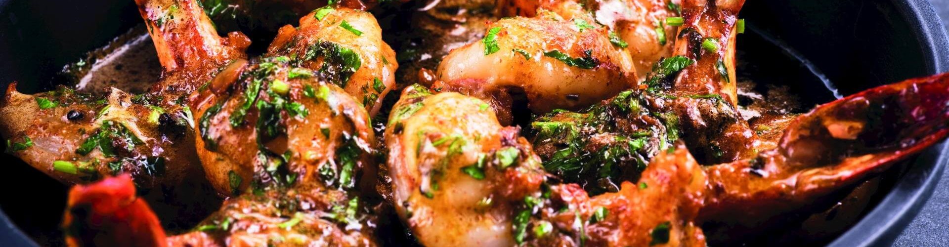 Un primo piano di gamberi alla cajun guarniti con prezzemolo in un piatto da portata nero, che mette in evidenza la ricca salsa e i colori vivaci.