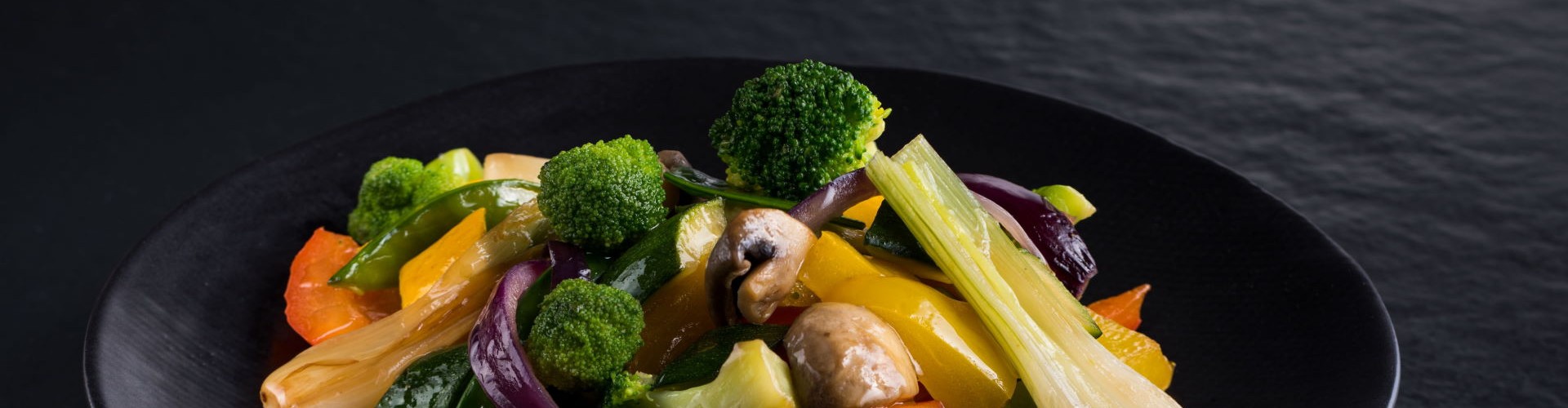 A vibrant plate of stir-fried vegetables, including broccoli, bell peppers, and mushrooms, presented on a black dish.