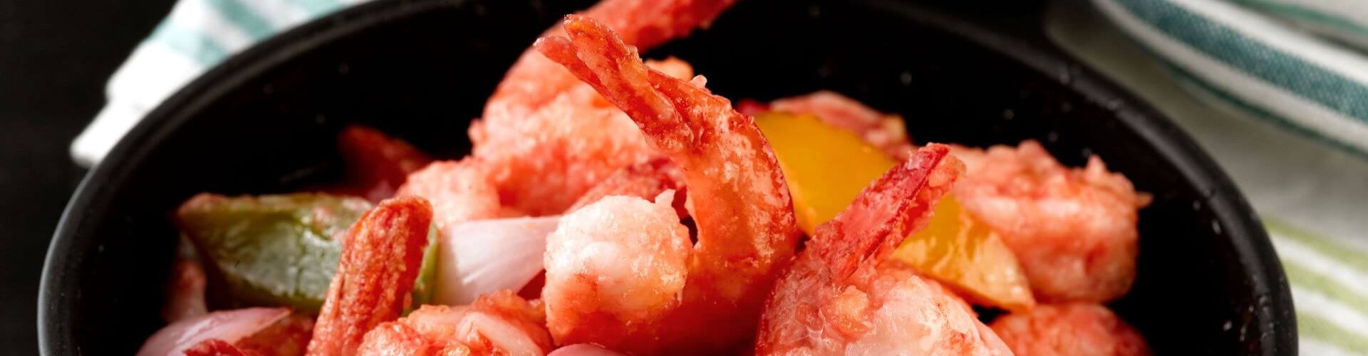 A bowl of sweet and sour prawns, featuring shrimp mixed with colorful bell peppers and onions.