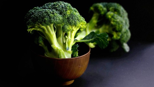 A bowl filled with fresh broccoli on a dark background, highlighting its vibrant green color and texture.