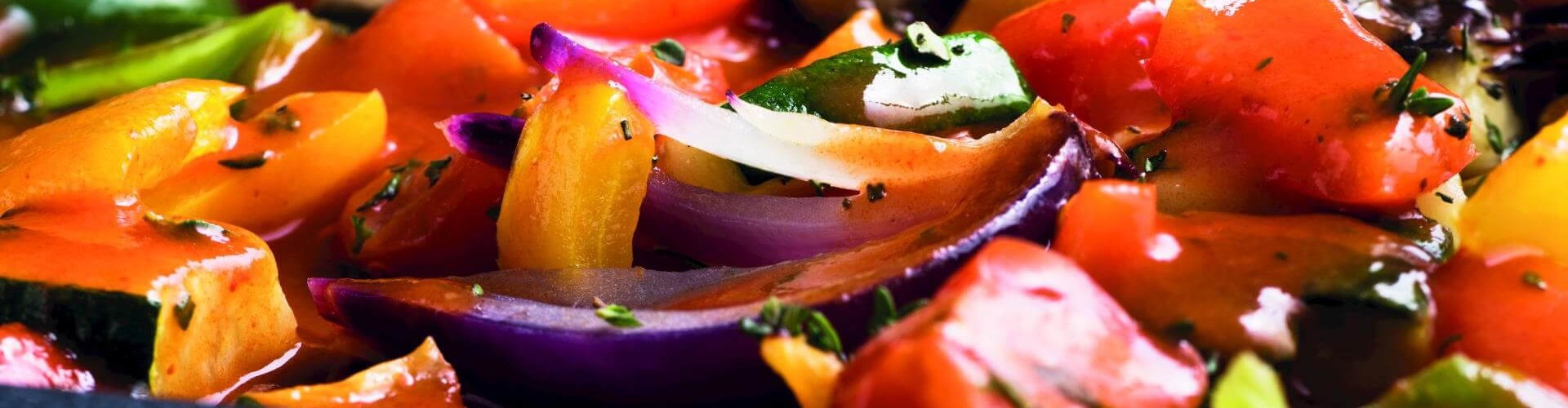 Gros plan sur un plat de ratatouille coloré composé d‘un mélange de poivrons, de courgettes et d‘oignons, le tout nappé de sauce.