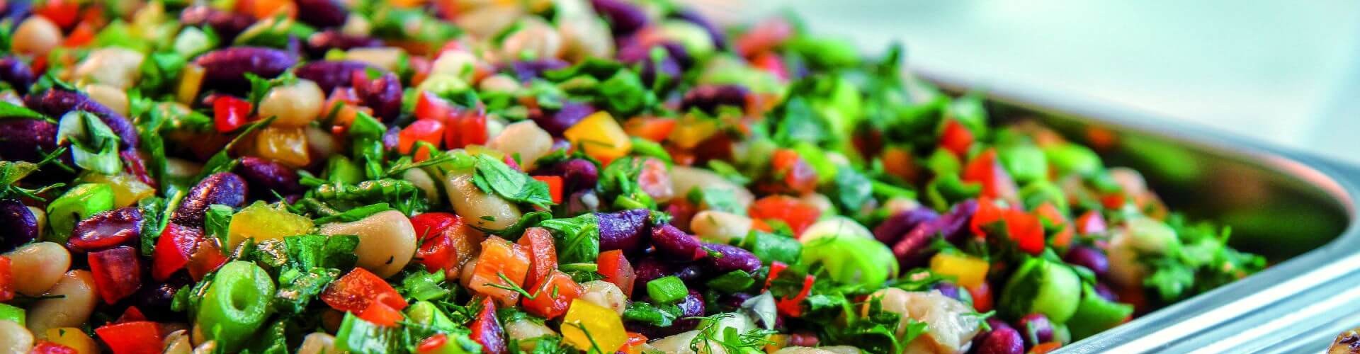 A vibrant bean salad with bell peppers, onions, and herbs in a tray, alongside grilled fish fillets with lemon slices.