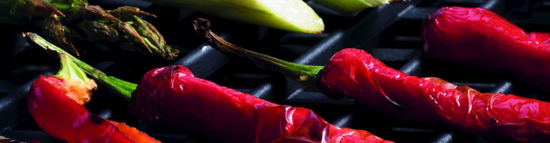 Close-up of grilled vegetables, including red chili peppers and asparagus, on a grill.