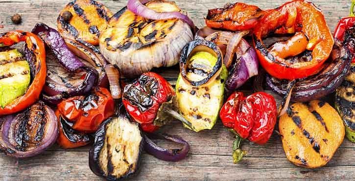 Assortiment de légumes grillés comprenant des poivrons, des aubergines et des oignons, disposés sur une surface en bois.