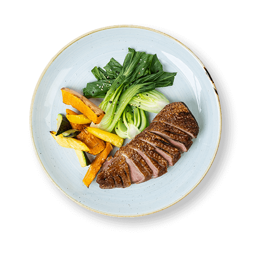 Plate of sliced duck breast served with pak choi and roasted vegetables.