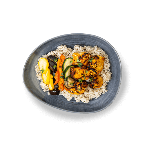 Plate of tandoori chicken served over rice with grilled vegetables.