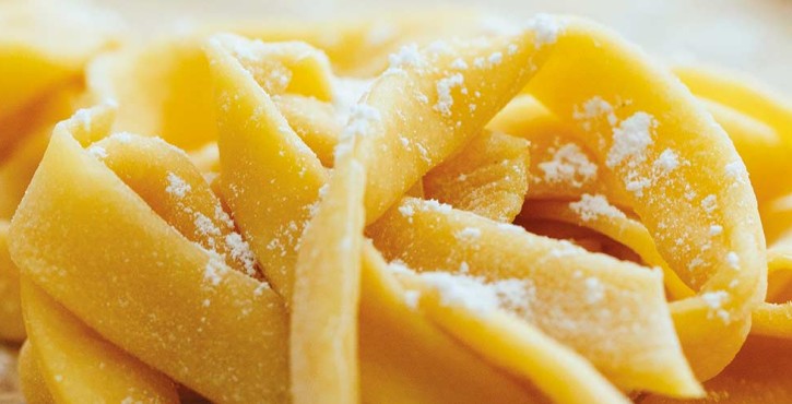 Primer plano de masa de pasta recién hecha, moldeada en delicados nidos y ligeramente espolvoreada con harina.